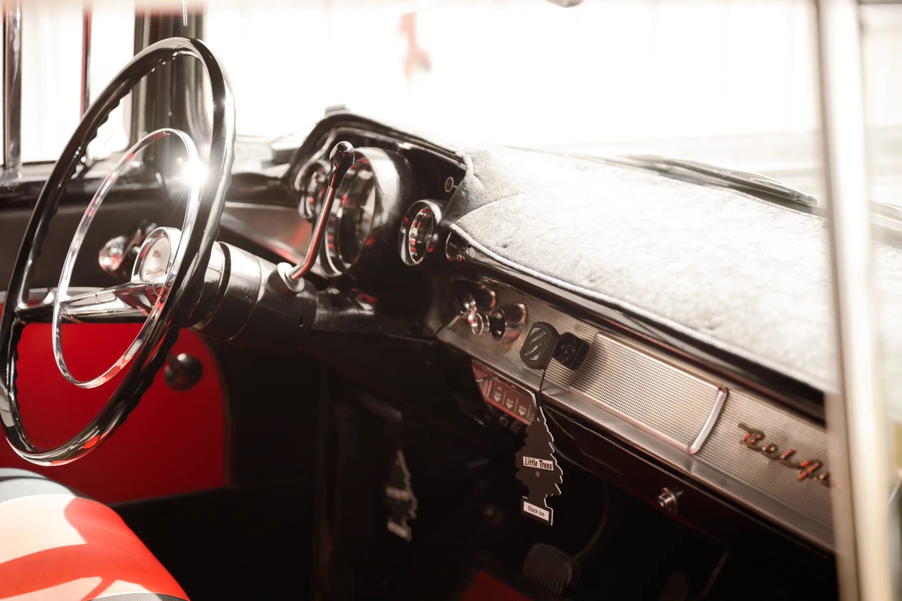 The chrome steering wheel and red and black dash of a classic Chevy Bel Air parked near the barn