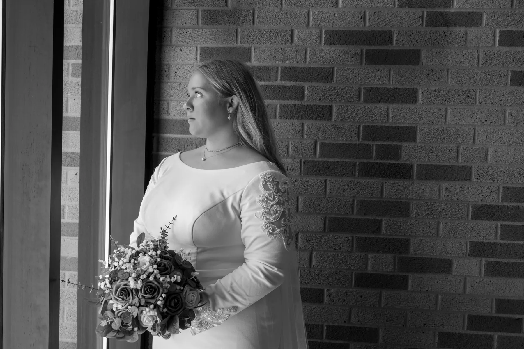 Kamryn standing alone at a tall window before the ceremony, her bouquet of dusty blue and white roses held loosely at her side
