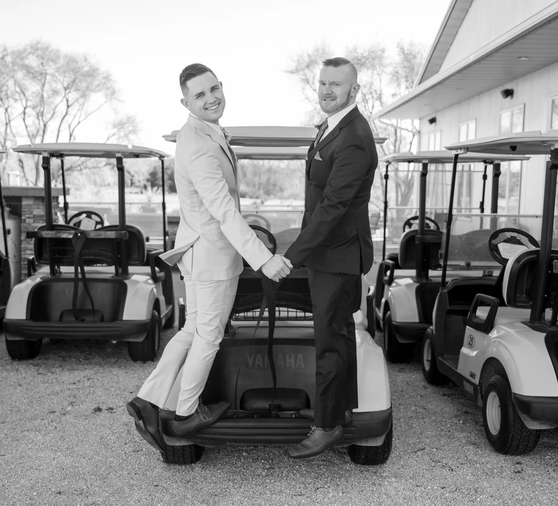 Devon and Joshua on the back bumper of a golf cart, hands held, grinning back at the camera