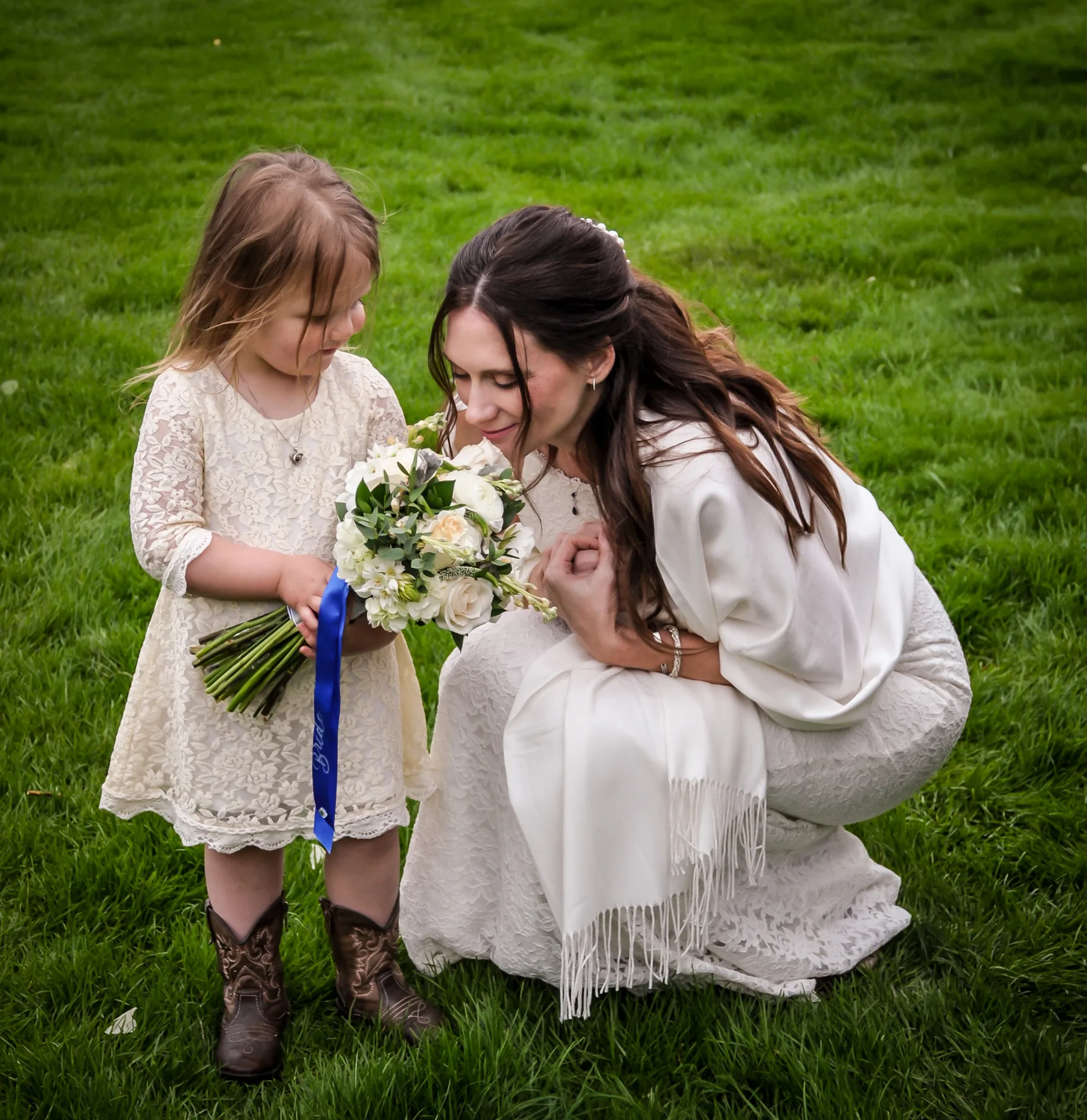 Rebecca crouched down to the flower girl on the green lawn, both in white lace, the little one in cowboy boots
