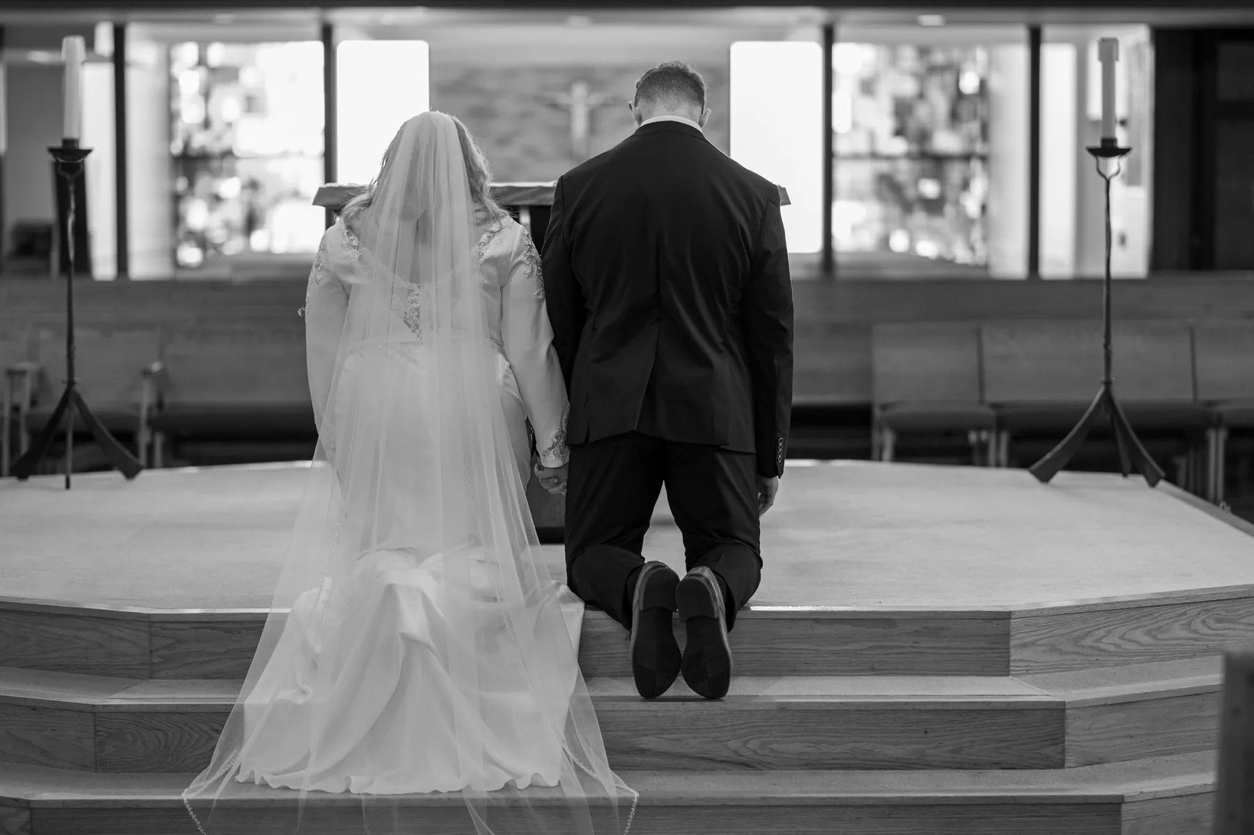 Kamryn and Isaiah kneeling at the altar steps, hands just touching, her veil falling long behind her