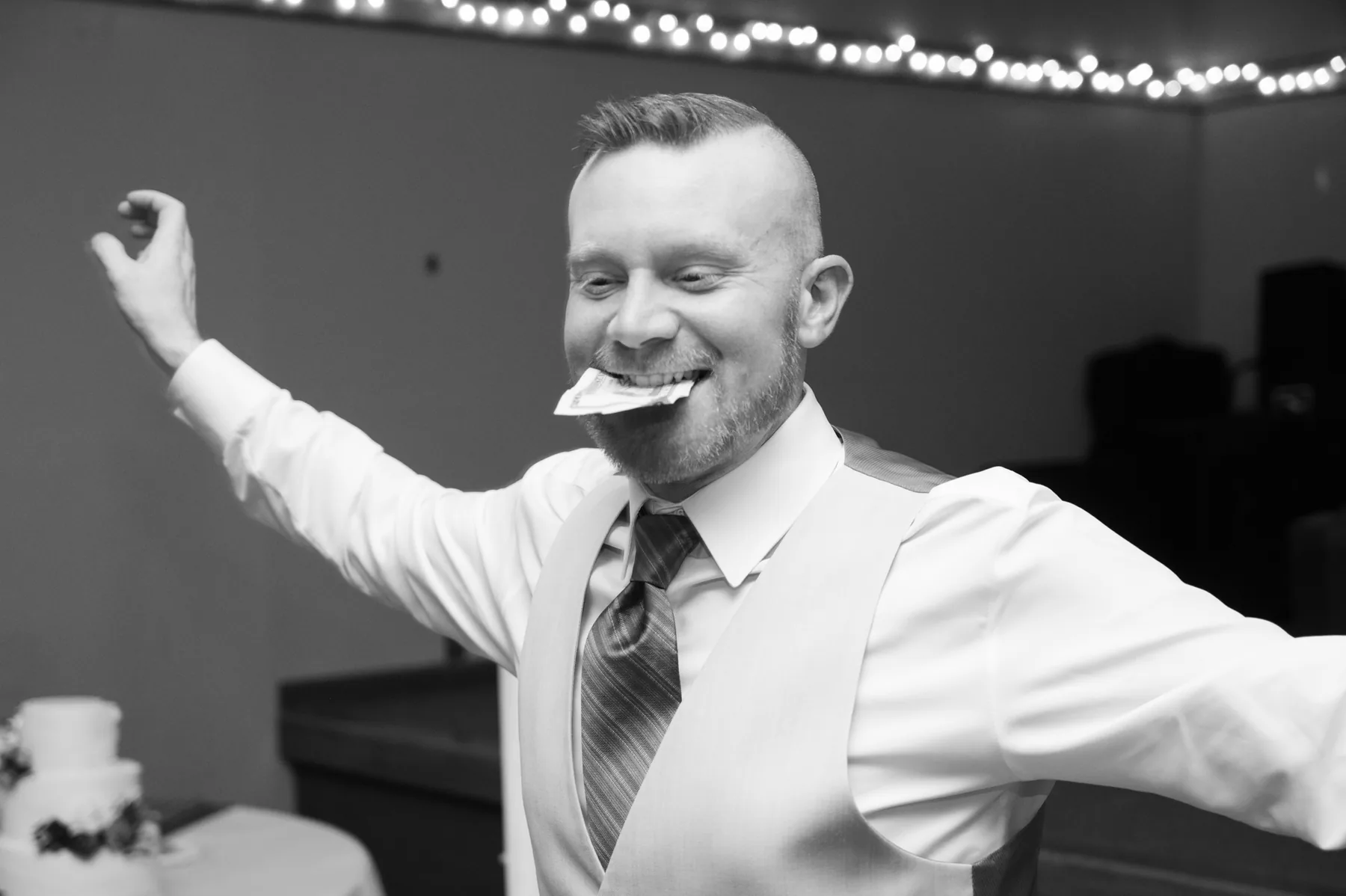 One of the grooms taking the dance floor with his arms flung wide under strung lights