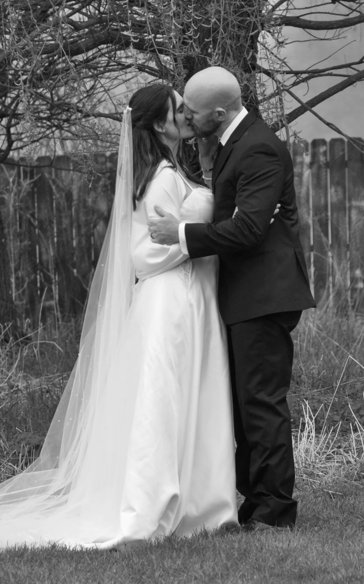 Rebecca and Dave's first kiss beneath bare branches, his arms around her and her veil catching the wind