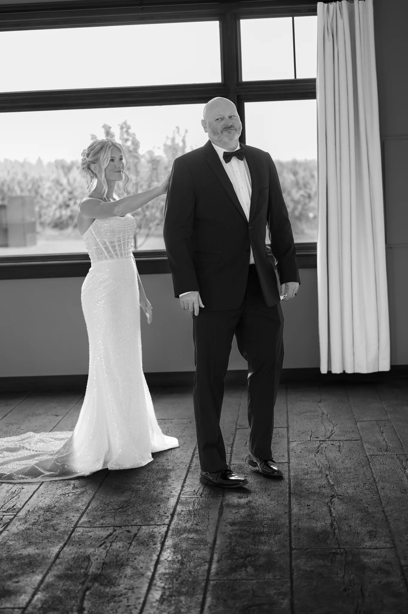 Rylee reaching for her father's shoulder as he turns for their first look, the window behind them