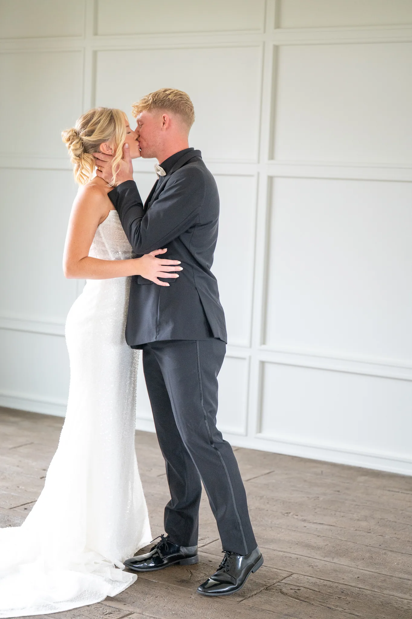 Rylee and Gage kissing in front of a white panelled wall, his hand at her cheek