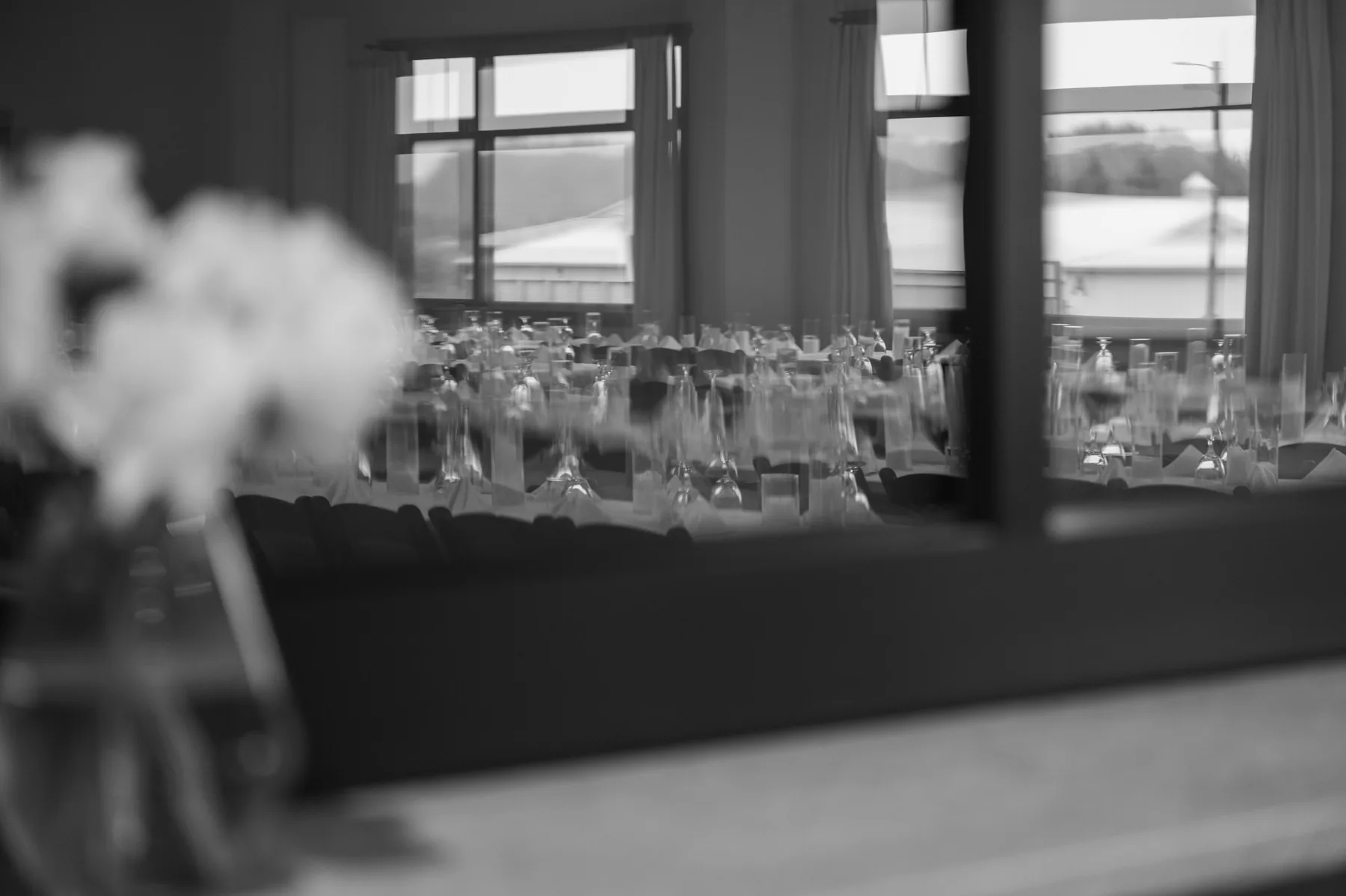 Black and white view through the doorway into the reception hall, glassware set out along the long tables