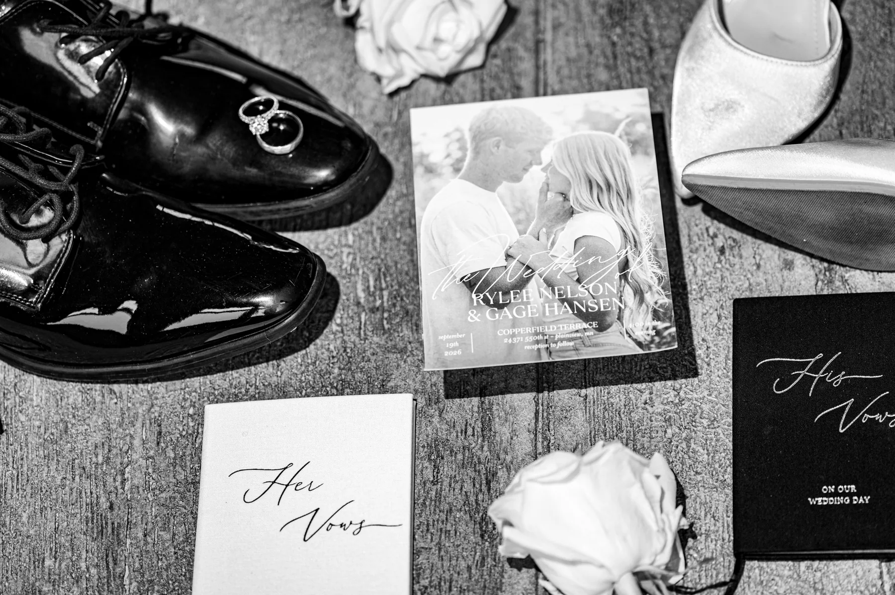 Black and white flat lay of shoes, rings, the invitation suite and vow books