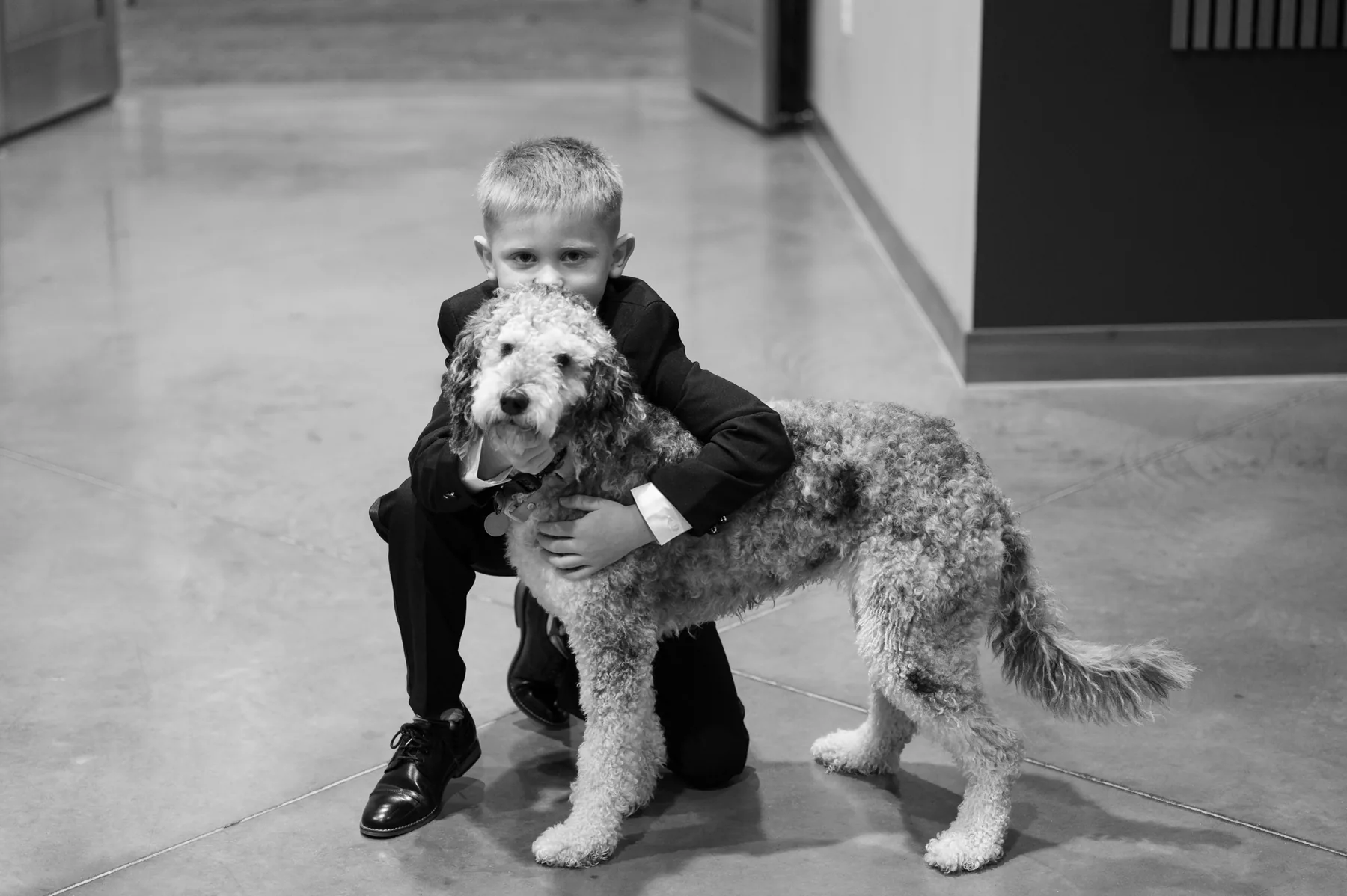 Ring bearer in a black suit hugging the family dog before the ceremony